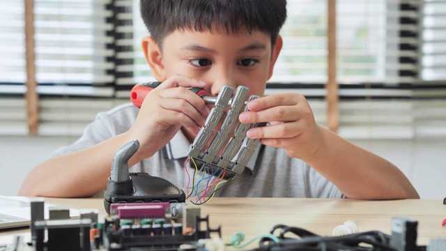 男孩在家里用电脑制作和编程，并制作一个机器人手臂作为学校的科学项目。他对自己的工作非常满意。教育、儿童、技术、科学是人们的理念