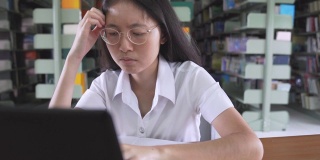 亚洲大学生女孩读书和工作用笔记本电脑和智能手机做她的家庭作业在公共图书馆