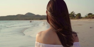 慢镜头-年轻的亚洲女子在海滩上散步。美丽的女性快乐放松漫步在海滩附近，日落在傍晚。生活方式女性旅行海滩概念。