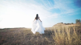 奔跑的新娘穿着令人惊叹的长裙穿过风景。视频素材模板下载