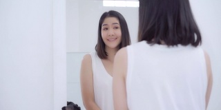 美丽的亚洲女人使用睫毛卷化妆前镜，快乐的女性使用美容化妆品提高自己准备在卧室在家里工作。生活方式女性在家放松的概念。