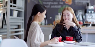 右图是两个年轻女性在咖啡馆一边喝咖啡一边愉快地聊天。红头发的女人情绪化地向她的亚洲朋友讲述故事