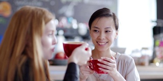 右图是两个年轻女人在咖啡馆喝茶或喝咖啡聊天的画面。亚洲女性讲述故事分散的白人朋友