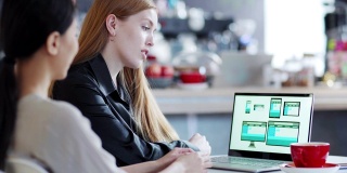 在咖啡馆的桌子上，一位红发女商人正在电脑屏幕上看亚洲设计师设计的网站模板