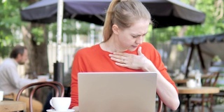 咳嗽的年轻女子坐在咖啡馆露台上用笔记本电脑工作