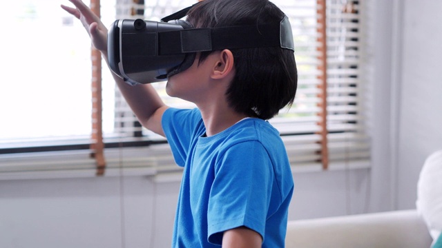 戴着虚拟现实眼镜的男孩。儿童体验虚拟现实。惊讶的小男孩看着VR眼镜。教育、儿童、技术、科学和人的观念