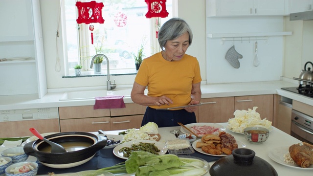 亚洲高级妇女在家用平板电脑做饭