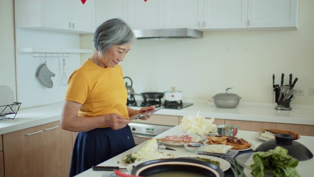 高级亚洲妇女在家烹饪在平板电脑上看食谱