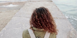 年轻的卷发黑发在手机上拍摄海景，从后面看，特写