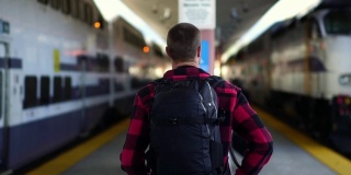 慢镜头:美丽的年轻男子走在洛杉矶火车站的站台上。千禧的概念在暑假，旅游冒险，城市生活方式。