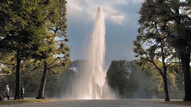 德国汉诺威。喷水池从放在地上的碗里喷出的巨大的高喷水池以公园里的绿树为背景。泌尿系统疾病和前列腺炎的治疗概念。慢动作