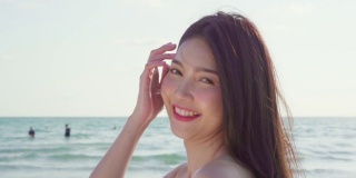 慢镜头-年轻的亚洲女子在海滩上散步。美丽的女性快乐放松漫步在海滩附近，日落在傍晚。生活方式女性旅行海滩概念。