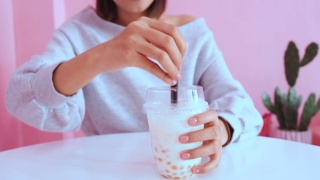 年轻的亚洲千禧一代女性在粉色柔和的咖啡馆喝冰珍珠奶茶视频素材模板下载