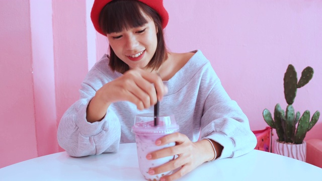 年轻的亚洲千禧一代女性在粉色柔和的咖啡馆喝冰珍珠奶茶