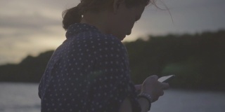 一个年轻女子在海边用智能手机的特写，慢镜头