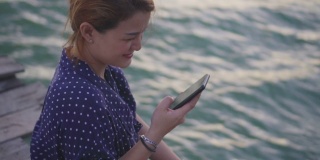 一个年轻女子在海边用智能手机的特写，慢镜头
