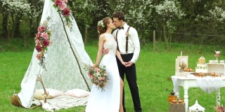 婚礼上的帐篷和新郎新娘在享受自然的桌子和蛋糕装饰。