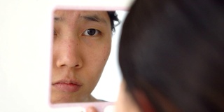 亚洲妇女观察她的青春痘通过手镜