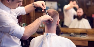 男子理发师在男子发廊用剪刀理发。剪裁过的男性客户向后坐着。镜面反射模糊