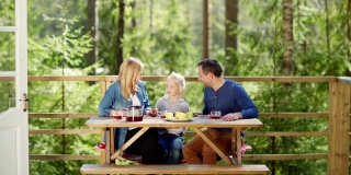一个充满爱的家庭，母亲，父亲和小女儿在乡村别墅门廊的木桌上喝茶，谈笑风生