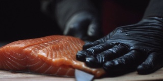 在寿司吧里，戴着手套的寿司厨师切鲜鲑鱼的特写。切三文鱼柳