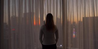 特写:兴高采烈的女人打开窗帘，看着夕阳下的城市。