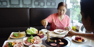 快乐的亚洲女人在热煤炉上烧烤猪肉。韩式或日式烧烤。