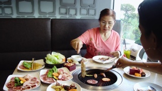 快乐的亚洲女人在热煤炉上烧烤猪肉。韩式或日式烧烤。视频素材模板下载