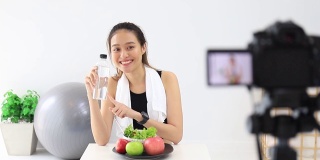 美丽的亚洲女人健康的博主展示了苹果水果和干净的减肥食品。在摄像机前录制在家的视频直播。在线社交媒体上的健身影响者。