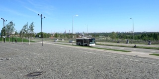 在阳光明媚的日子里，公共汽车沿着安静的校园石道旁边的空旷道路行驶。