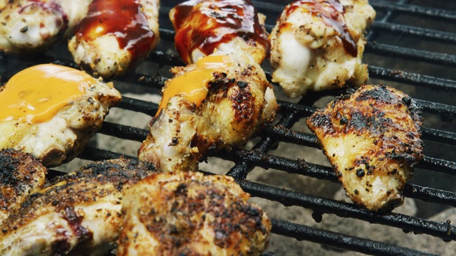 一个高加索人在一个户外烧烤架上用勺子把水牛城/辣酱浇在烹饪鸡翅上