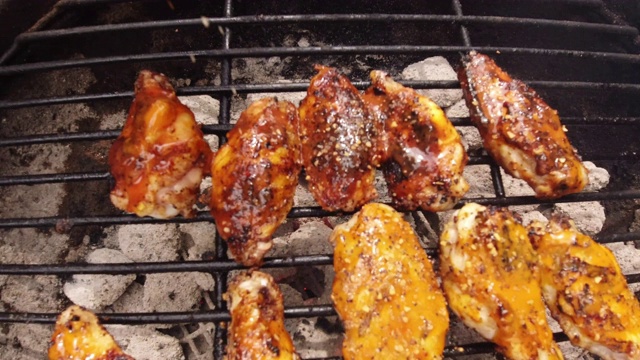将香料洒在户外烧烤架上点燃的木炭团上的金属格栅上腌制过的鸡翅上