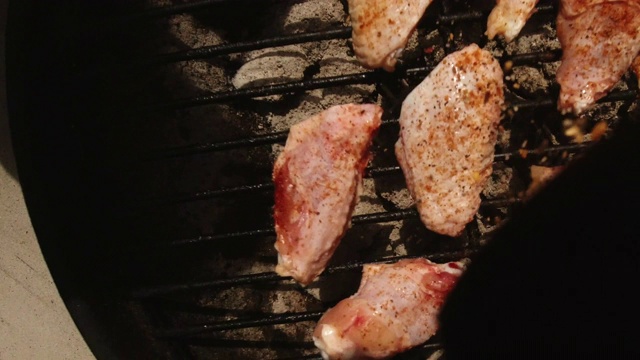 在户外烧烤架上的生鸡翅上直接洒上香草/调味料(从调味料容器的角度看)