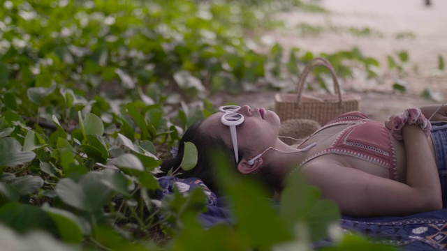 年轻女子躺在沙滩上享受戴上耳机的乐趣。