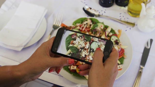 一名女性用4K特写镜头用智能手机拍摄她在餐厅吃健康沙拉的照片，并发布在社交媒体上