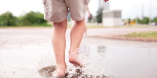 光着脚的小男孩跑进了城市街道的水坑里