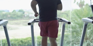 完全的男性在健身房的跑步机上跑步。减肥和运动的概念。后视图