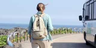 一个年轻的女游客背着背包走在有海景的路上。