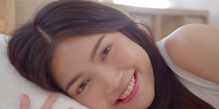 亚洲女人微笑躺在床上的卧室，美丽的日本女性使用放松时间后，在家里醒来。生活方式女性在家里使用放松时间的概念。慢动作镜头。
