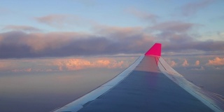 飞机在海洋和热带岛屿上空的云层上飞行。清晨日出与机翼的飞机