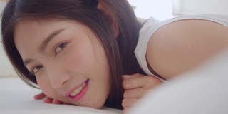 亚洲女人微笑躺在床上的卧室，美丽的日本女性使用放松时间后，在家里醒来。生活方式女性在家里使用放松时间的概念。