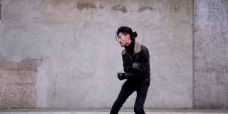 一名留着小胡子的中国青年在城市混凝土墙旁的街道上跳舞。他穿着夹克，看起来有点笨拙，4k镜头，慢动作。