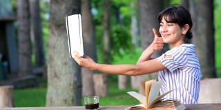 一个年轻的女人在户外拿着书、咖啡和平板电脑的肖像