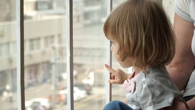 Сlose金发小女孩和奶奶坐在家附近的窗台上，望着窗外大城市的马路。