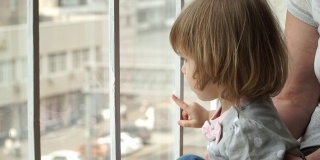 Сlose金发小女孩和奶奶坐在家附近的窗台上，望着窗外大城市的马路。