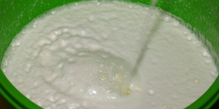 牛奶正被倒进一个绿色的桶里。牛奶从黄色的管子里以细流的形式流出来。自制黄油。