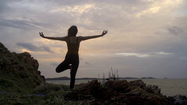 4k/年轻的亚洲苗条女子瑜伽在日落的海滩上，日出的背景。健身、运动、瑜伽、剪影、健康理念。