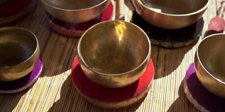 一名亚洲神药女大师表演藏式碗疗愈仪式的超慢镜头。用西藏唱碗冥想。她坐在凉亭里冥想，背景是美丽的瀑布