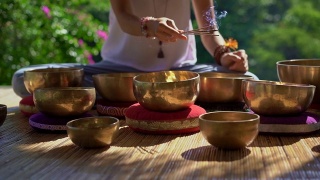 一名亚洲神药女大师表演藏式碗疗愈仪式的超慢镜头。用西藏唱碗冥想。她坐在凉亭里冥想，背景是美丽的瀑布视频素材模板下载