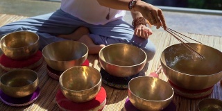 一名亚洲神药女大师表演藏式碗疗愈仪式的超慢镜头。用西藏唱碗冥想。她坐在凉亭里冥想，背景是美丽的瀑布